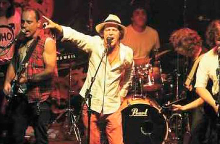 Foto com a banda It’s Only Rolling Stones, com o vocalista Keta na frente, cantando ao microfone no placo